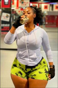 Woman drinking from a cup while wearing neon green shorts and black fingerless gloves.
