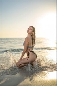 a woman is sitting on a beach with a surfboard
