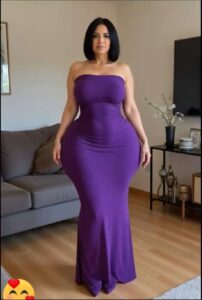 A woman in a purple strapless gown stands indoors in a living room. A gray couch, a dark side table with decorative items, and a flat-screen television are visible in the background.