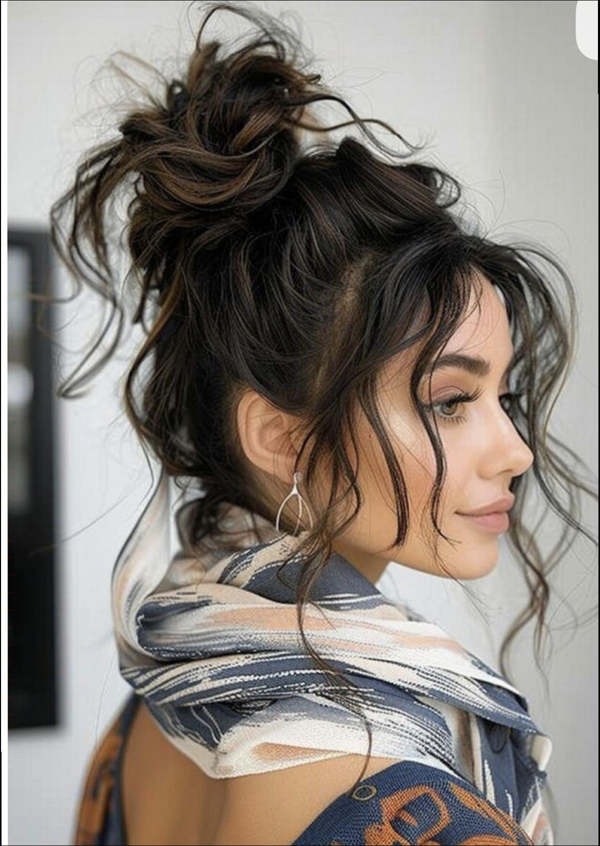 A woman with a messy updo wears a patterned scarf and dangling earrings. Her dark hair is styled with loose curls framing her face, and she looks over her shoulder against a plain background.