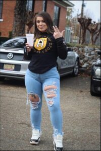 Woman in athletic wear holding a drink and making a peace sign.